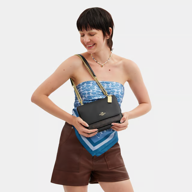 Woman holding a black Coach handbag against a white background