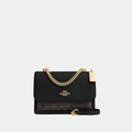 Black handbag with gold chain and Coach logo on a white background