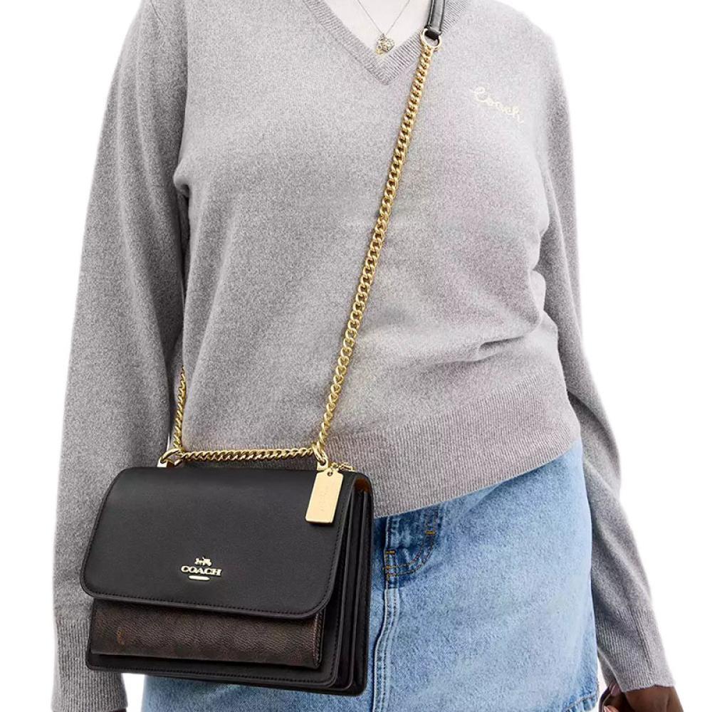 Person wearing a gray sweater and blue jeans with a black Coach handbag on a white background